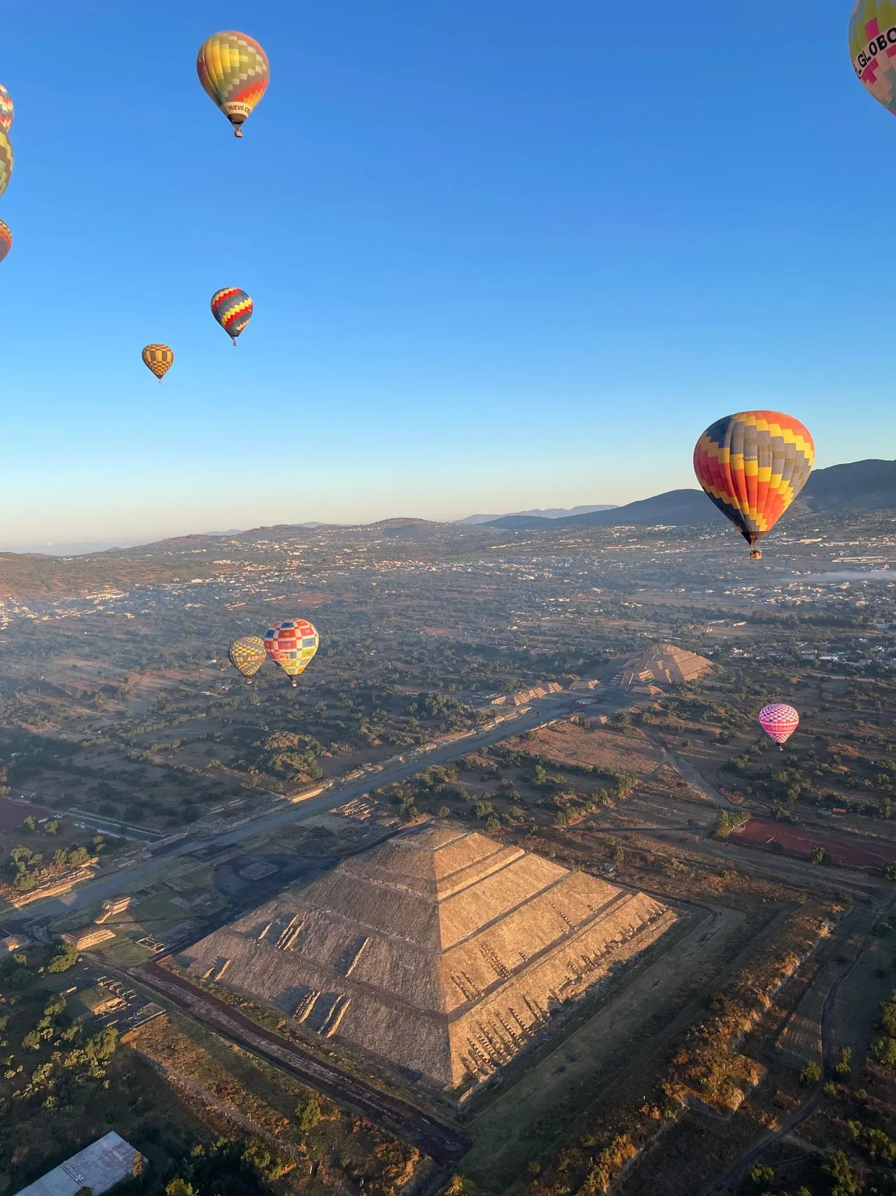 Dozens of hot air balloons drifting above the pyramids of Teotihuacán at sunrise