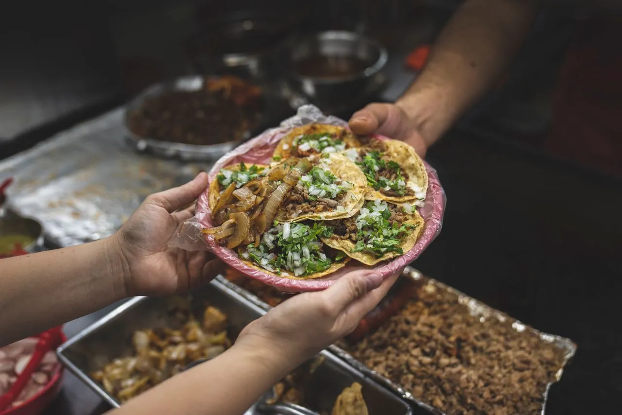 Street tacos topped with chopped onion and cilantro served on a plate in Mexico City